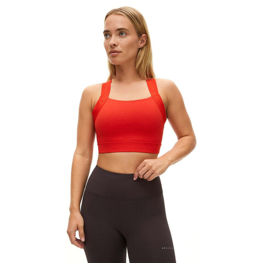 A person stands against a white background wearing a red Rohnisch Kay Sports Bra and dark, high-waisted leggings made from recycled polyester.