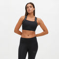 A person poses with hands on hips in black workout attire featuring the Rohnisch Kay Sports Bra, known for its breathable fabric and branded straps, set against a plain white background.
