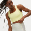 A person with long braids wears a Rohnisch Kay Sports Bra and leggings, crafted from moisture-wicking recycled polyester, standing against a plain background.