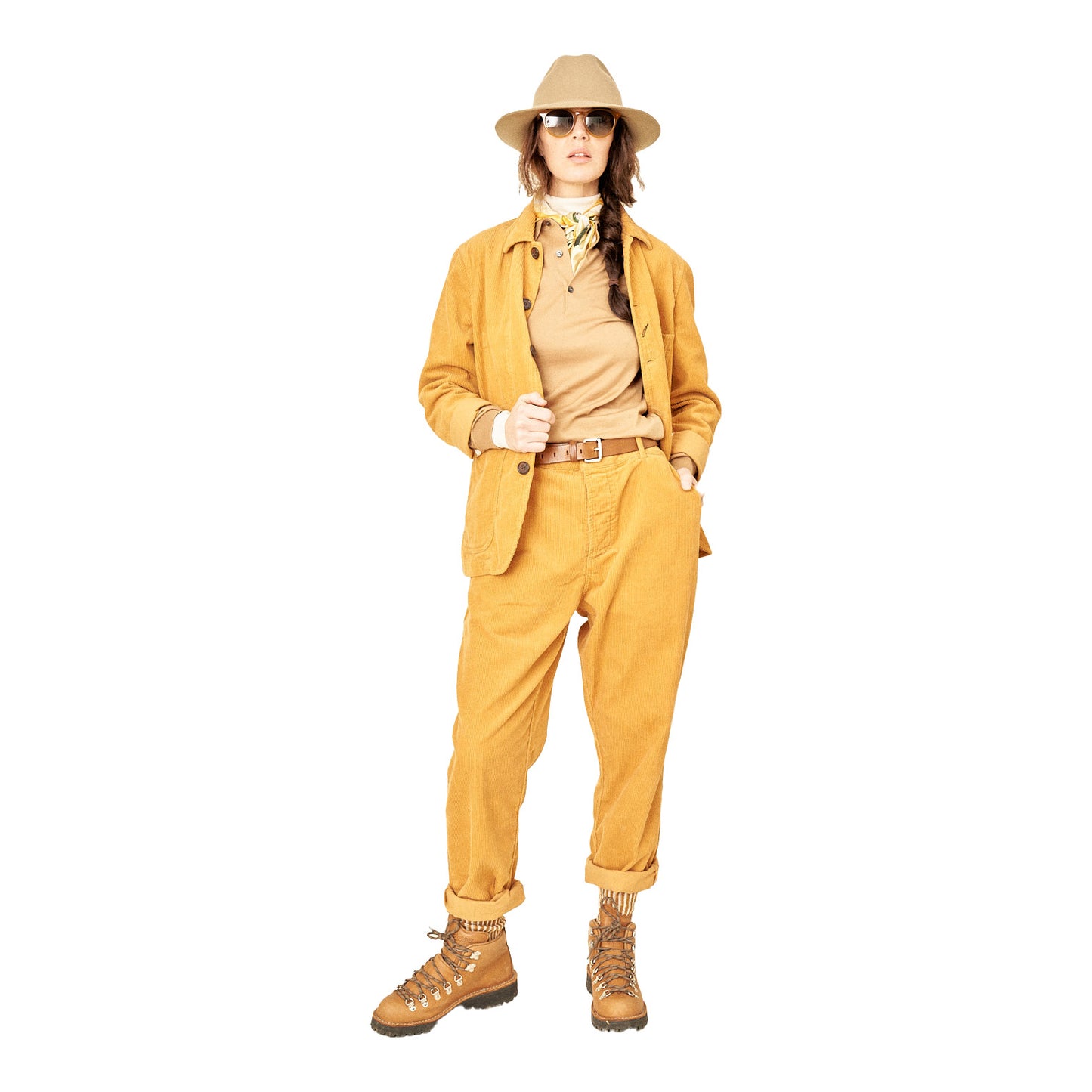 Dressed in Universal Works' Military Chino Corduroy pants in a rich corn hue, matched with a soft corduroy hat and sunglasses, this person showcases a relaxed hiking style on a plain white backdrop.
