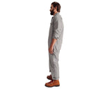 A man with a beard and tied-back hair stands in profile, wearing a Climbing Jumpsuit, Light Grey-1 by Westerlind made of cotton ripstop fabric and brown work boots.