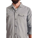 A person wears a light gray, buttoned-up Climbing Jumpsuit, Light Grey-1 from Westerlind made of cotton ripstop with two front pockets, ensuring ease of mobility. Their face is not visible.