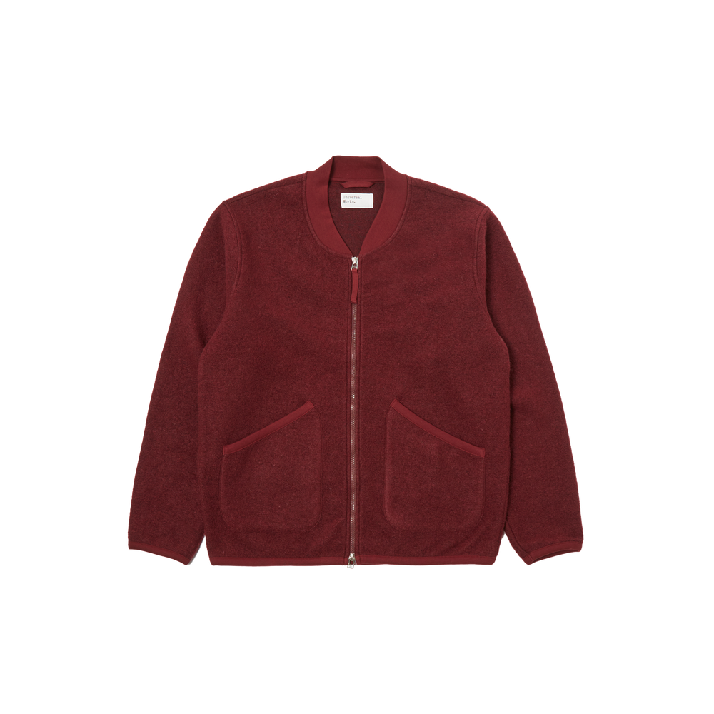 Universal Works introduces the Zip Bomber Fleece, a red jacket designed with a two-way zip and a simple collar. It is crafted in a regular fit and includes two front pockets for practicality.